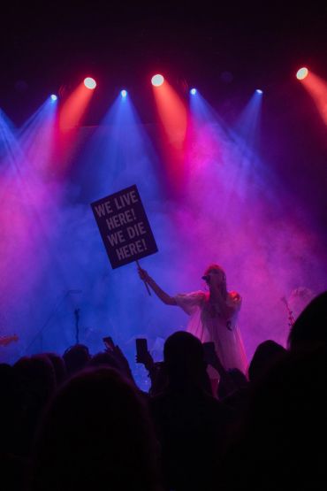 Performer holding a sign with a message during a colorful concert.