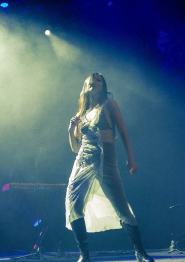 Female performer dancing on stage in dramatic lighting.