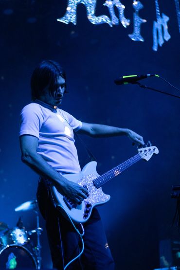 Musician playing bass guitar on stage under blue lighting.