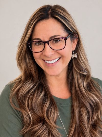 Smiling woman with long hair and glasses.