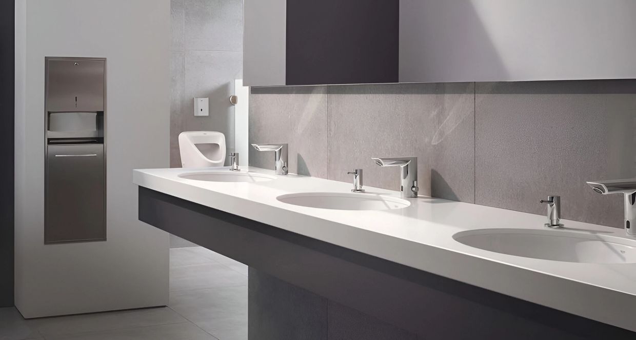Image of a commercial bathroom found in a commercial building, showing sensor sinks and a urinal.