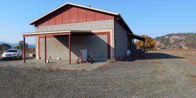 A large barn-like building with a gravel driveway and scenic hills in the background.