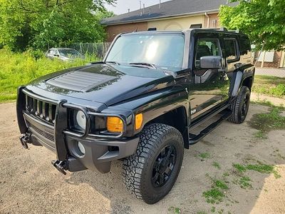Black Hummer H3 parked on a driveway surrounded by greenery.