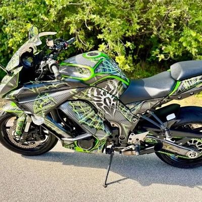 Sport motorcycle with green and black tribal design parked on road.
