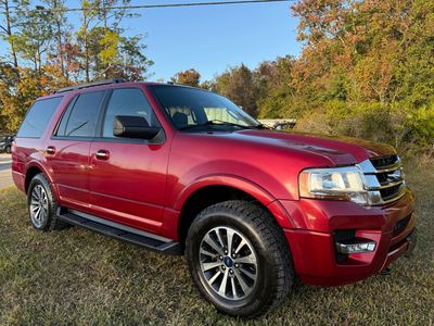 Red SUV parked on grass with autumn trees in background.