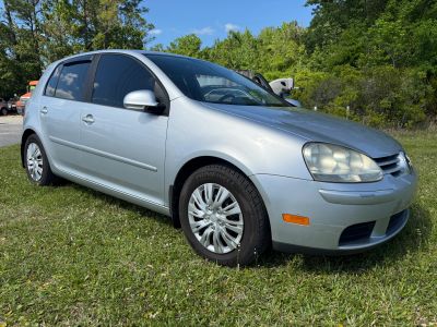 Silver hatchback car parked on grass with trees in background.