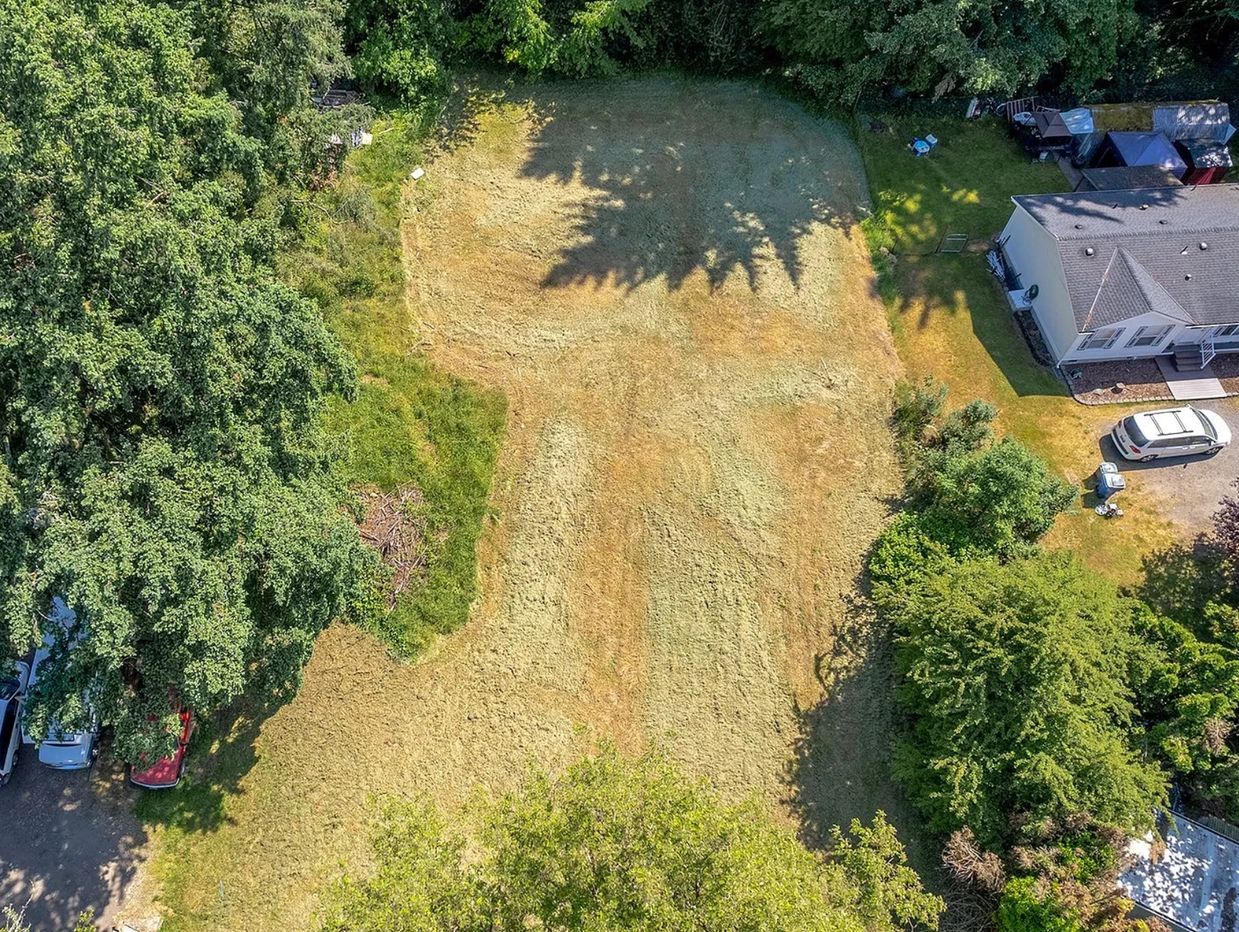 Aerial view of a grassy field next to a house and surrounded by trees.