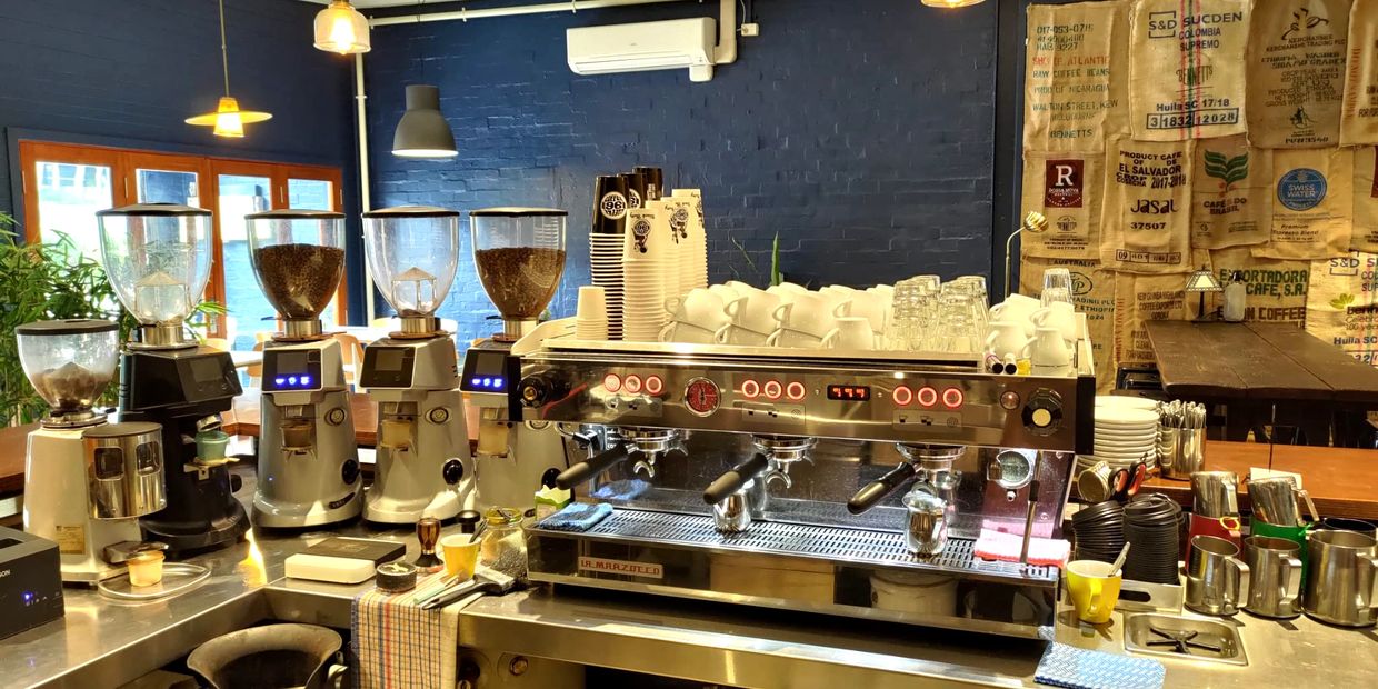 La Marzocco coffee machine and warmly lit cafe with coffee bean bags on the wall