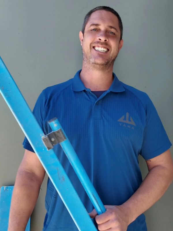 Man smiling while holding a blue ladder against a gray wall.