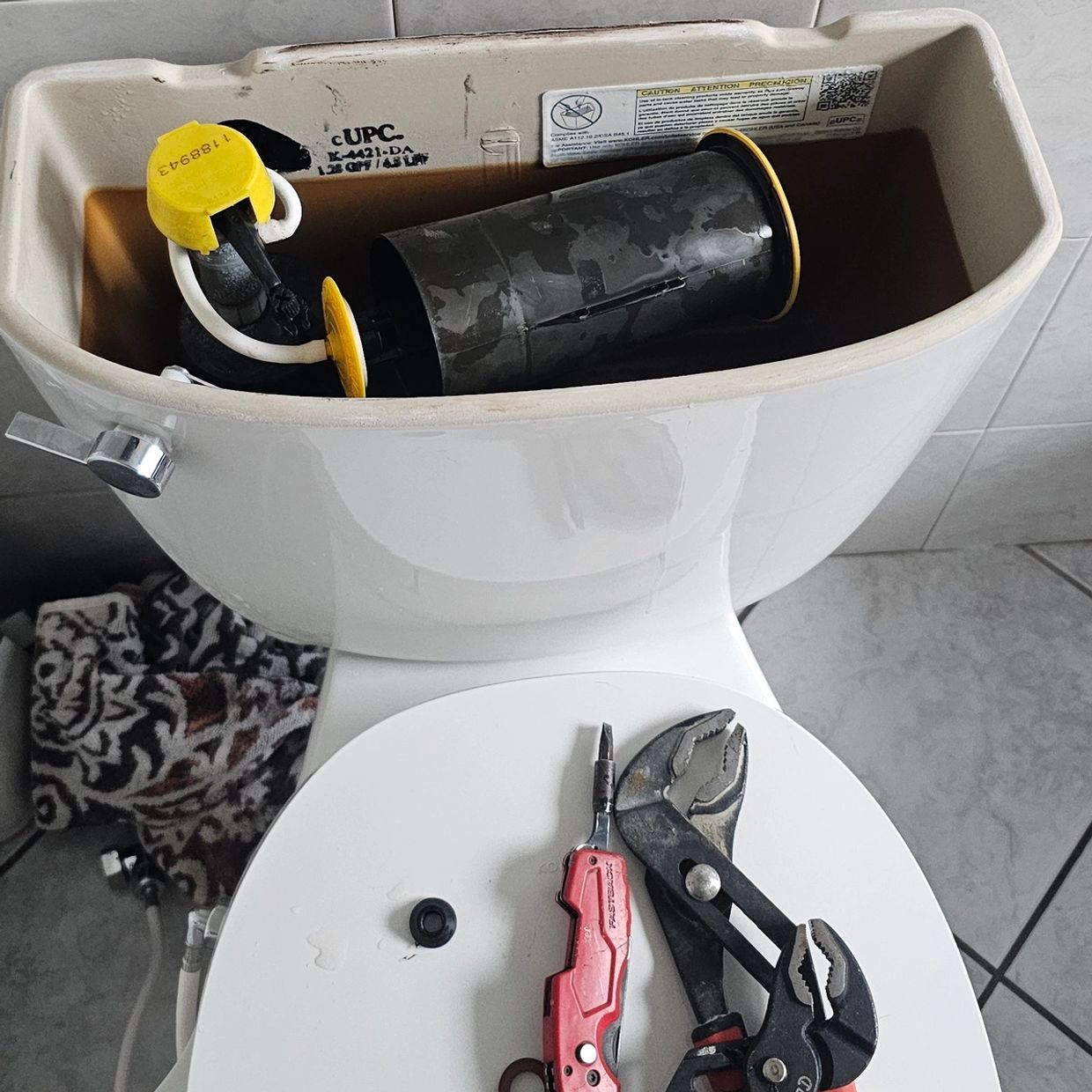 Open toilet tank with tools on the closed seat in a bathroom.