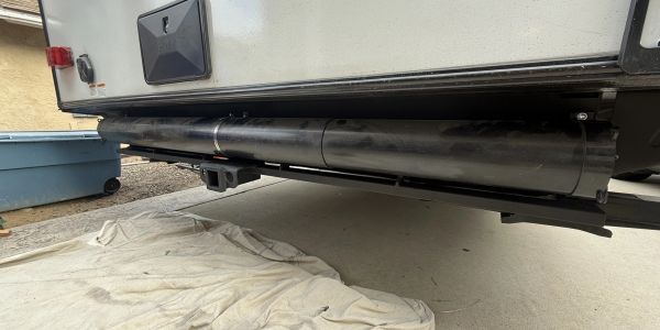 Black cylindrical pipe installed under a vehicle near a tarp.