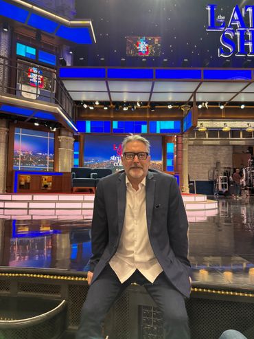 Man in suit sitting on stage at The Late Show set.