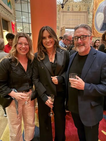 Three people dressed formally, holding drinks at an indoor event.