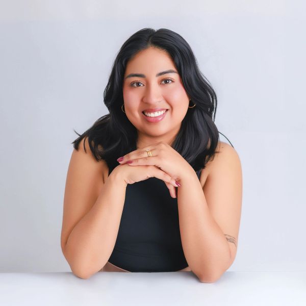 Smiling woman with black hair resting her chin on folded hands.