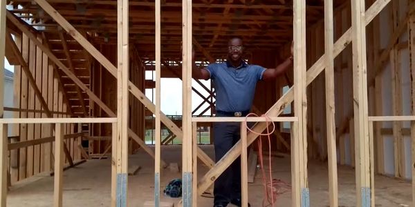 Man standing inside a wooden house frame under construction.