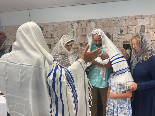 A family participates in a traditional Jewish ceremony with prayer shawls and head coverings.
