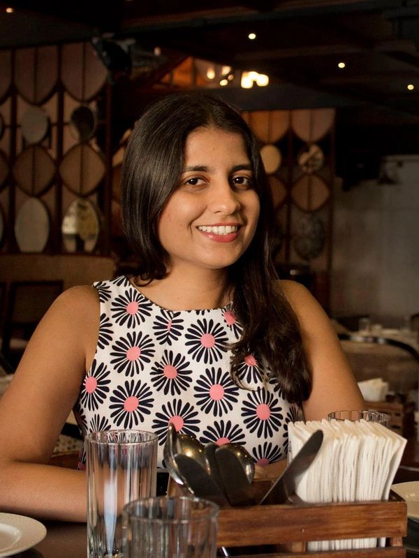 Smiling woman in a floral dress seated at a restaurant table.