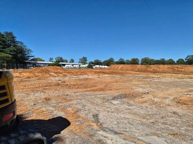 Cleared construction site under a clear blue sky with some machinery visible.