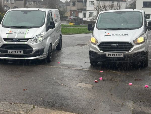 Two white company vans parked on wet pavement in rainy weather.