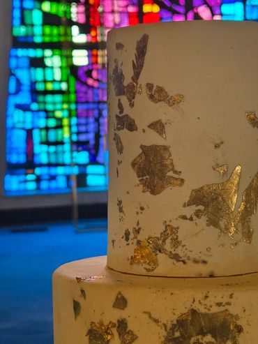 Cake with gold leaf decoration and colorful stained glass background.