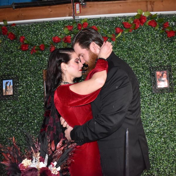 Couple embraces lovingly in front of a floral wall.
