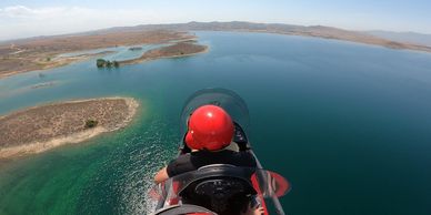 Person flying a red-helmeted aircraft over a large lake with islands.