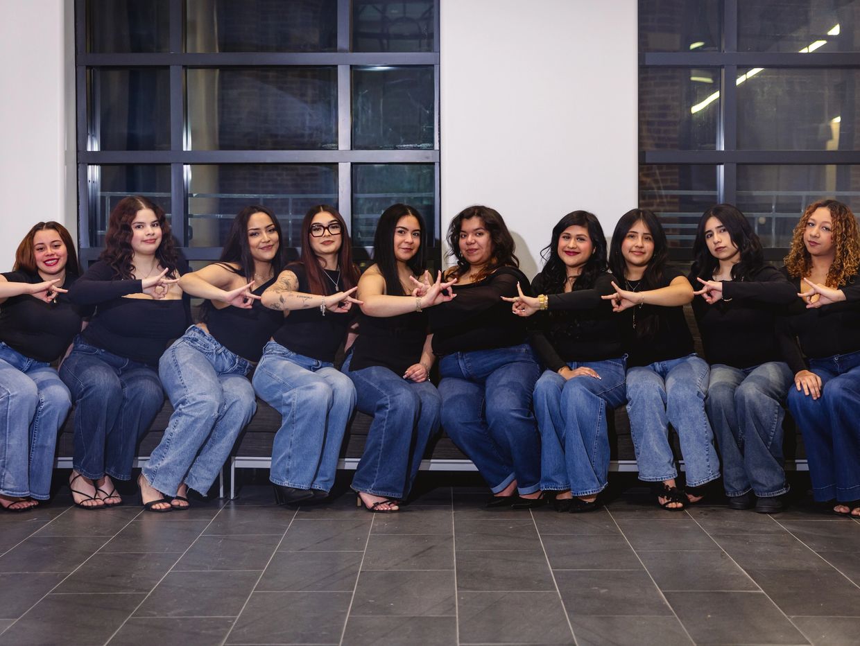 A group of women in black tops and jeans sitting together making hand signs.