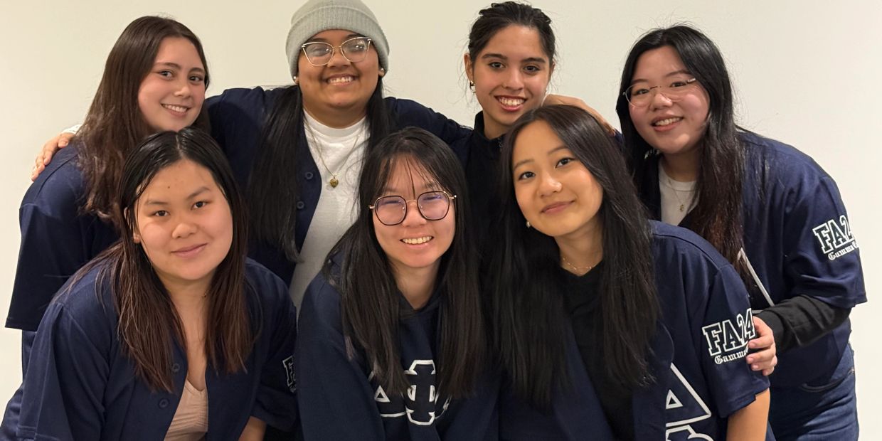 A group of seven young women smiling together, wearing matching navy blue shirts.