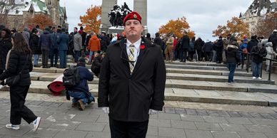 Man in black coat and red beret stands before crowd on stone steps.