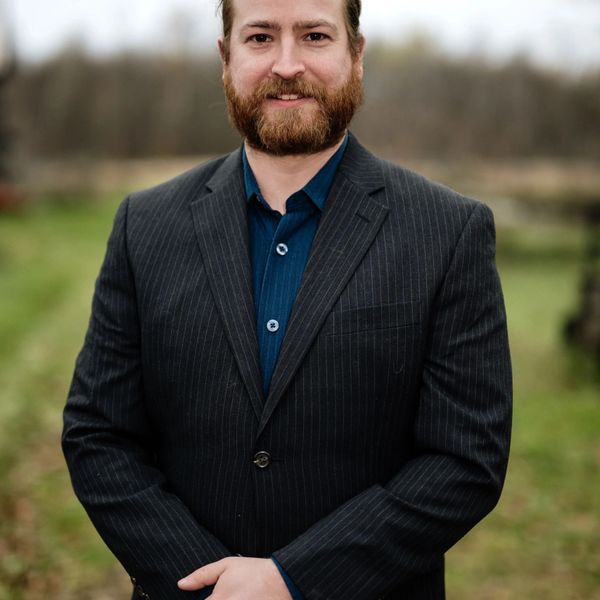 Male Paralegal with a pinstripe suit stands before a red brick wall