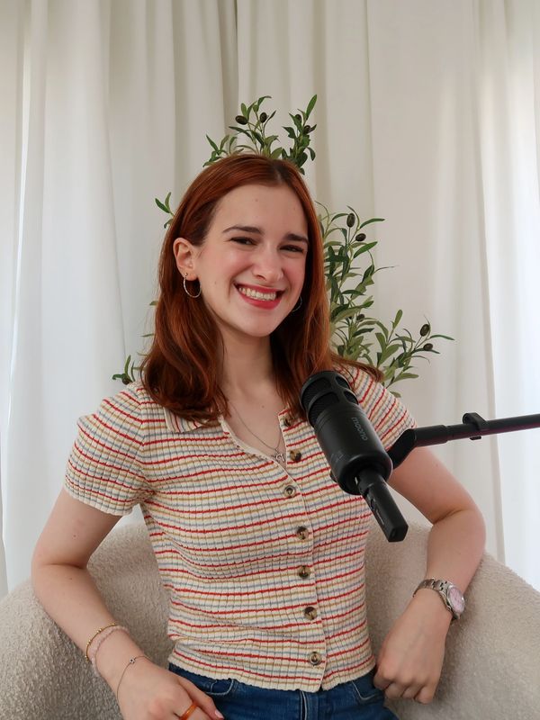 A smiling young woman with red hair sits beside a microphone, ready to speak.