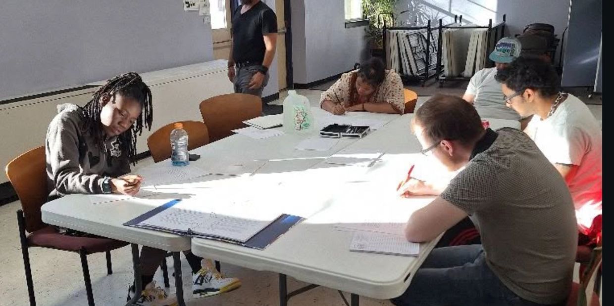 Group of people focused on writing at a table in a bright room.