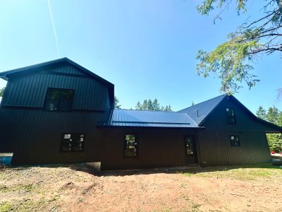 Modern black house with metal roof under clear blue sky.
