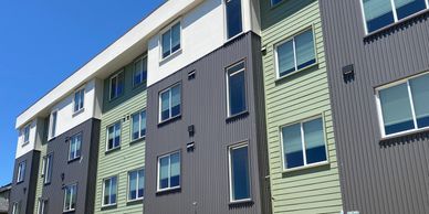 Modern apartment building with mixed green and gray siding under blue sky.