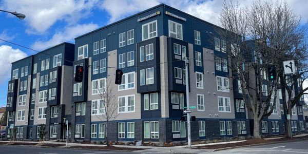 Modern apartment building on a city corner with traffic lights and clear skies.