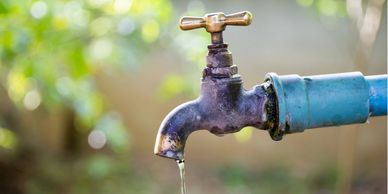 Rusty outdoor water tap dripping water with a blurred green background.