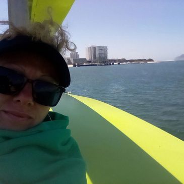 Person wearing sunglasses on a boat with city skyline in the background.