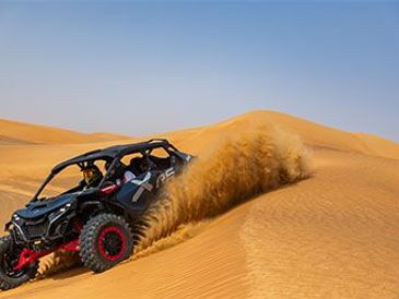 Off-road vehicle kicking up sand in desert dunes.