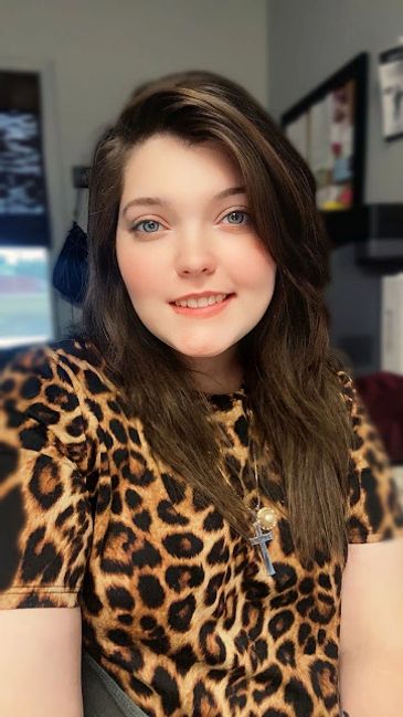 Young woman with blue eyes wearing a leopard print shirt and cross necklace.