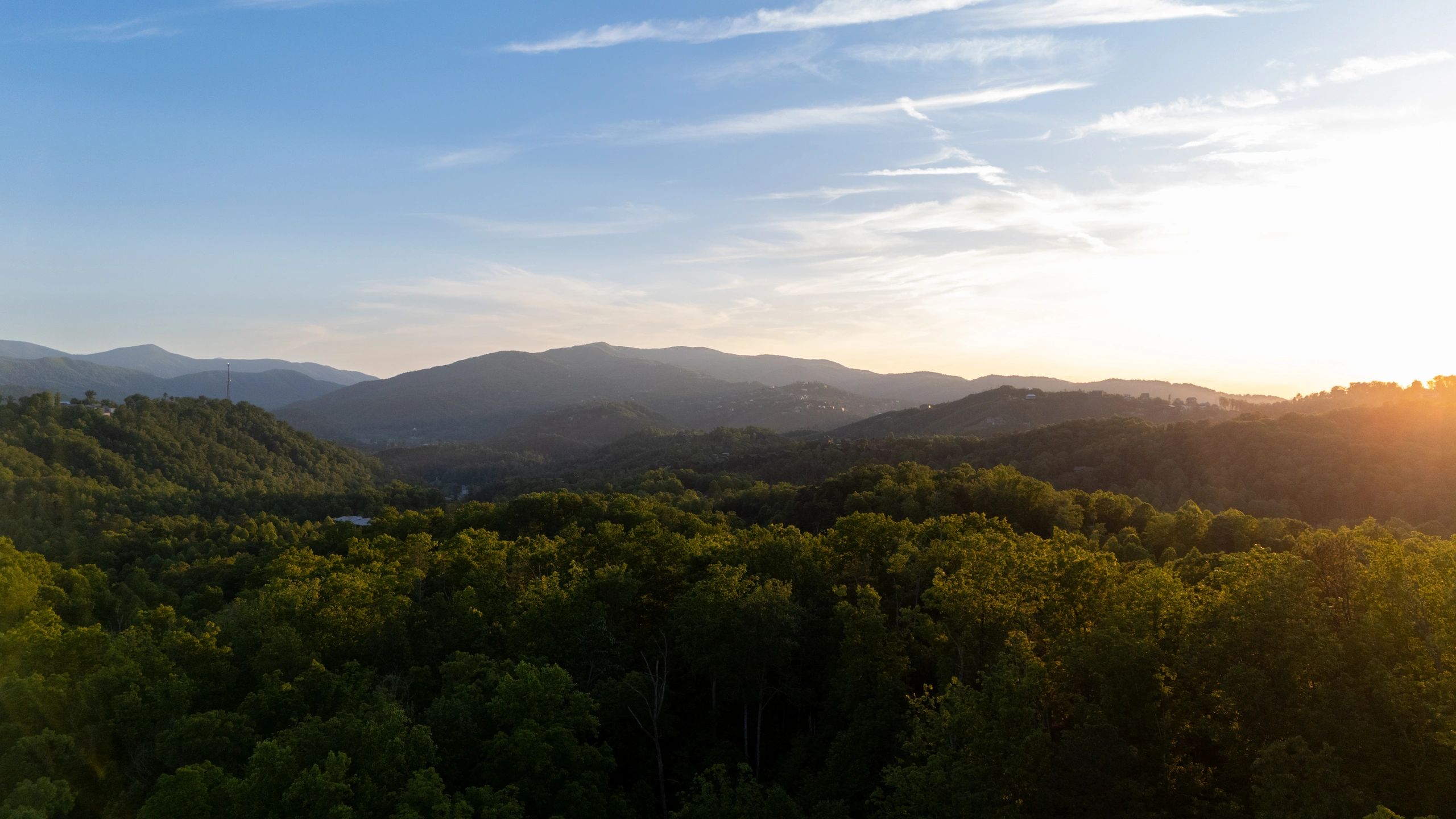 Sunset over a lush green mountain range with a clear blue sky.