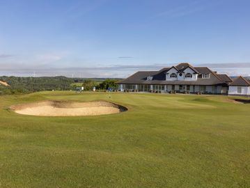 Golf course with sand bunker and clubhouse under blue sky.