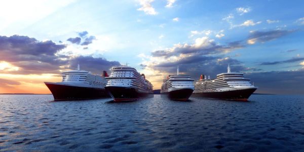 Four cruise ships sailing side by side on calm ocean waters at sunset.