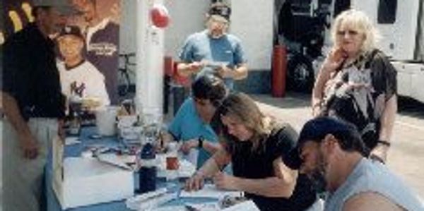 People signing autographs at a table outdoors.