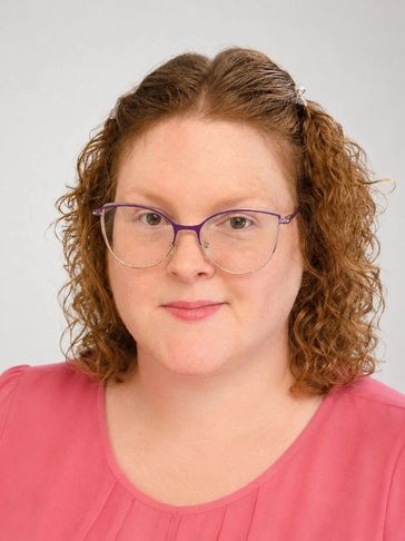 Woman with curly hair and glasses in a pink top.