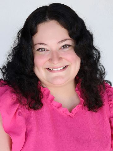 Woman with dark curly hair in a pink blouse smiling.