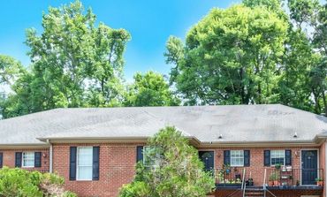 A brick house with black shutters and a tree in front.