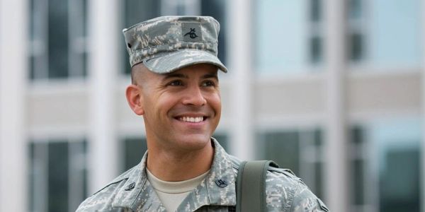 Smiling U.S. Army soldier in uniform carrying a bag outdoors.