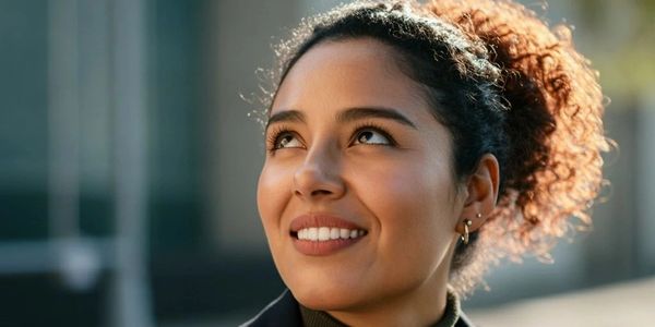 Confident woman smiling and looking upward outdoors in business attire.