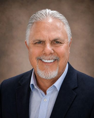 Smiling older man with gray hair and beard in a professional suit.