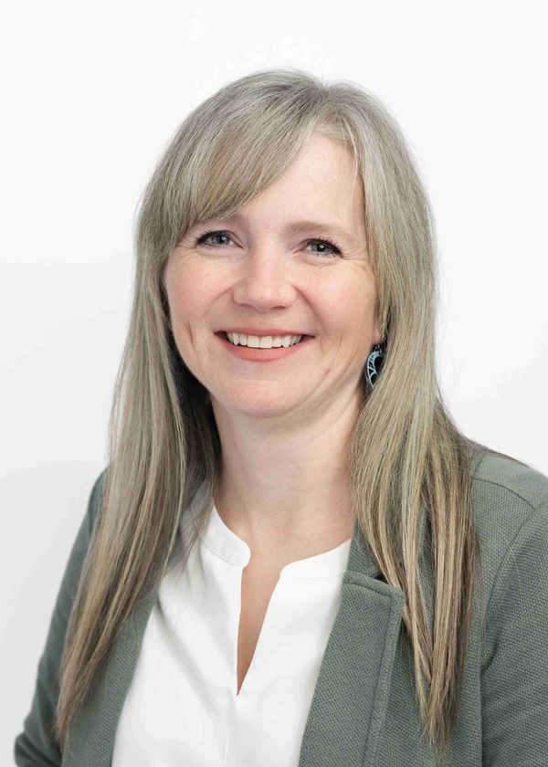 Smiling woman with long blonde hair and green jacket.